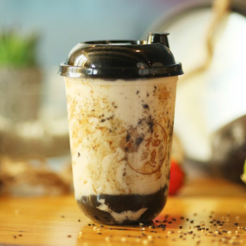 Un thé au lait au sésame noir dans un gobelet au logo 栖息, perles de tapioca au fond